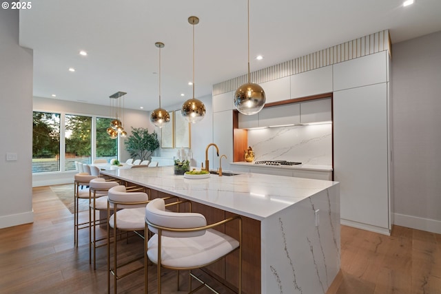 kitchen with decorative light fixtures, white cabinetry, sink, decorative backsplash, and a spacious island