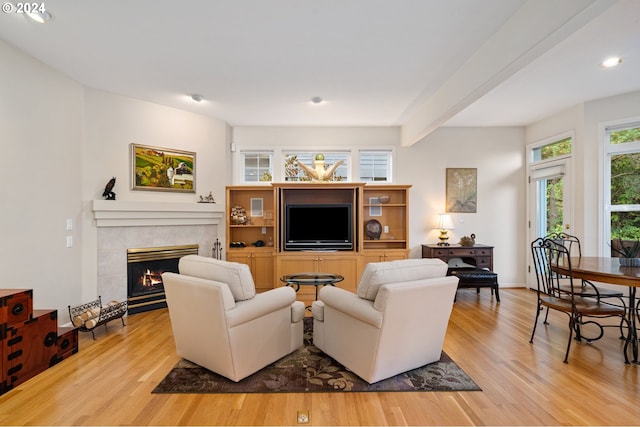 living room with beam ceiling, light hardwood / wood-style floors, and a tile fireplace