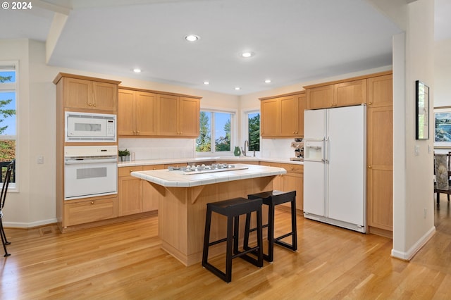 kitchen featuring light hardwood / wood-style floors, a kitchen island, a kitchen breakfast bar, white appliances, and tile countertops