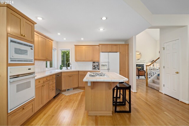 kitchen with white appliances, a kitchen island, a breakfast bar area, light hardwood / wood-style flooring, and tile counters