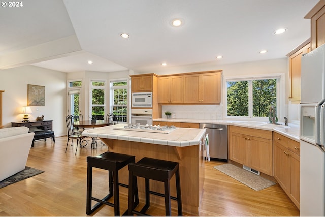 kitchen with light hardwood / wood-style flooring, tile counters, white appliances, and a healthy amount of sunlight