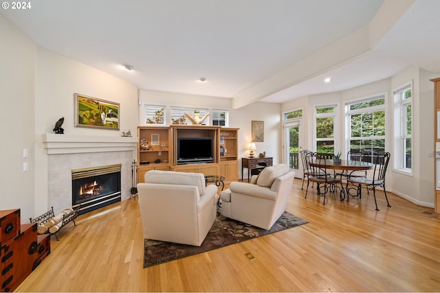 living area with recessed lighting, a wealth of natural light, a tile fireplace, and light wood-type flooring