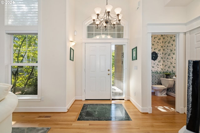 entryway featuring baseboards, visible vents, an inviting chandelier, light wood-style floors, and a high ceiling