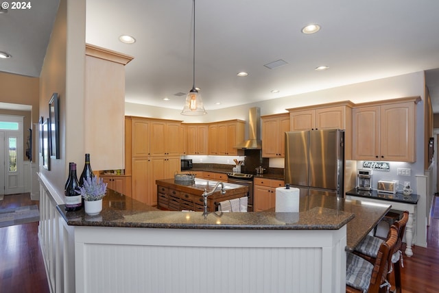 kitchen with light brown cabinets, dark hardwood / wood-style flooring, kitchen peninsula, stainless steel appliances, and wall chimney range hood