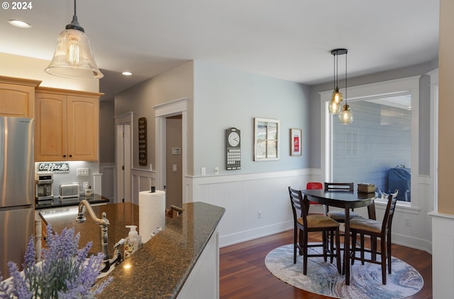 kitchen with pendant lighting, dark wood-type flooring, dark stone countertops, and stainless steel refrigerator