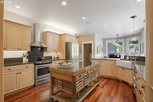 kitchen featuring pendant lighting, light brown cabinetry, stainless steel appliances, and wall chimney exhaust hood