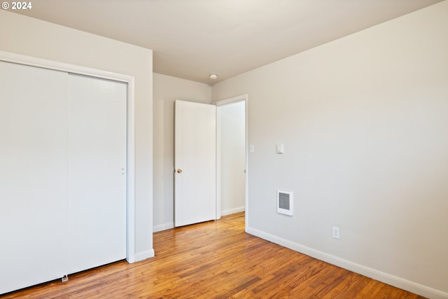 unfurnished bedroom with light wood-type flooring, heating unit, and a closet