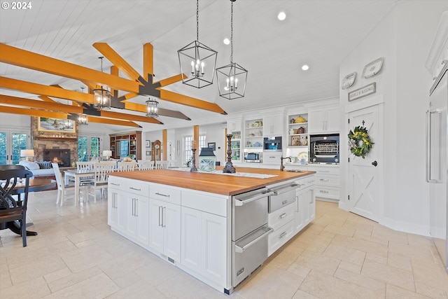 kitchen featuring wooden counters, a center island, pendant lighting, a fireplace, and white cabinets