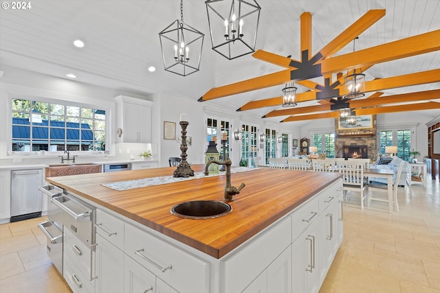 kitchen with decorative light fixtures, a kitchen island, wooden counters, white cabinets, and vaulted ceiling with beams