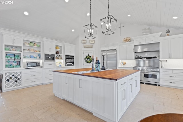 kitchen featuring hanging light fixtures, an island with sink, high end appliances, white cabinetry, and butcher block counters