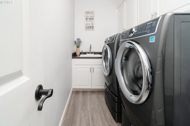 laundry area featuring cabinets, washing machine and clothes dryer, sink, and light hardwood / wood-style floors