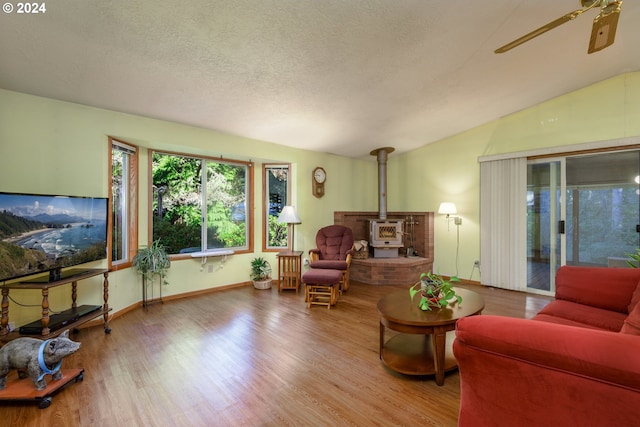 living area featuring a ceiling fan, lofted ceiling, wood finished floors, a wood stove, and a textured ceiling