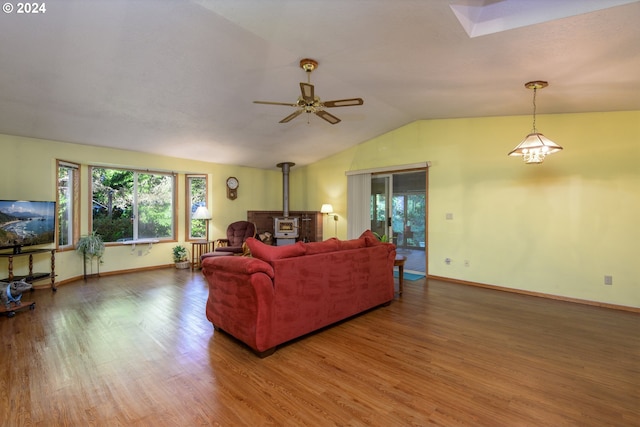 living area with vaulted ceiling with skylight, baseboards, ceiling fan, wood finished floors, and a wood stove