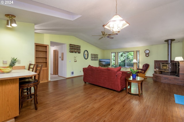 living area featuring lofted ceiling, wood finished floors, visible vents, a ceiling fan, and a wood stove