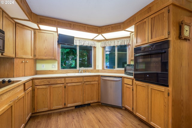 kitchen with a sink, light countertops, light wood-type flooring, brown cabinets, and black appliances