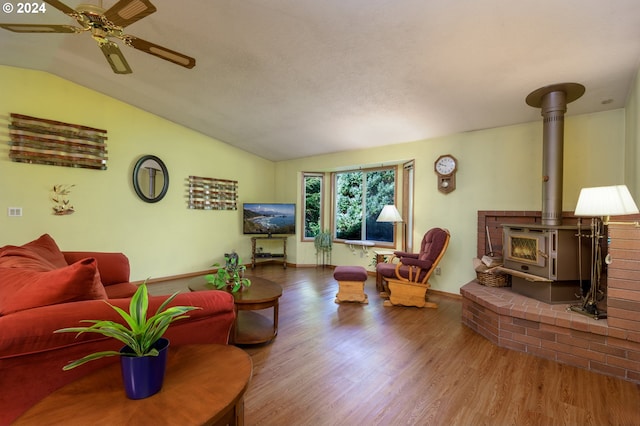 living area with lofted ceiling, ceiling fan, wood finished floors, and a wood stove