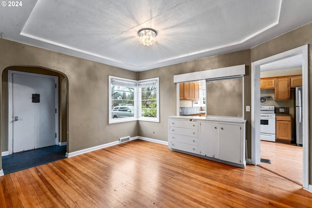 kitchen with white range with electric cooktop, light hardwood / wood-style floors, a textured ceiling, and stainless steel refrigerator