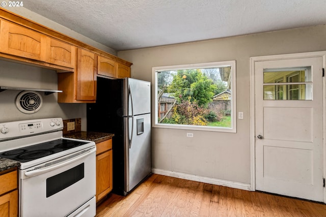 kitchen featuring stainless steel fridge, a textured ceiling, dark stone countertops, white electric range, and light hardwood / wood-style floors