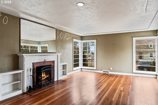 unfurnished living room featuring wood-type flooring, a textured ceiling, a wealth of natural light, and a tiled fireplace