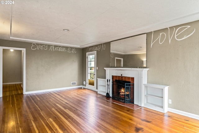 unfurnished living room with a tiled fireplace, a textured ceiling, and hardwood / wood-style flooring