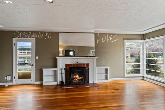 unfurnished living room with a tile fireplace, a textured ceiling, and hardwood / wood-style flooring