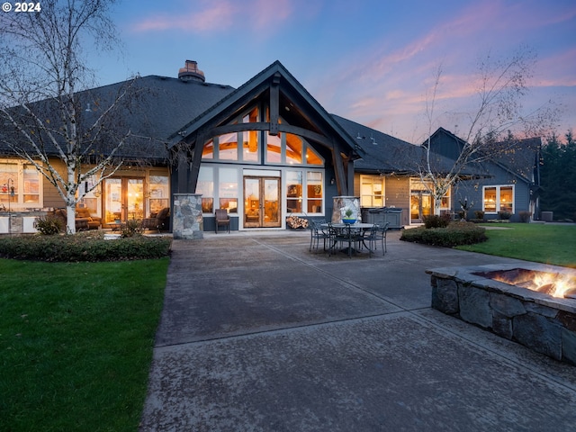 back house at dusk featuring a lawn, a patio area, an outdoor fire pit, and french doors