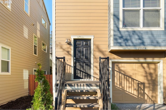 view of exterior entry with an attached garage and fence