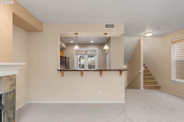 unfurnished living room featuring light colored carpet, a fireplace, visible vents, and stairs