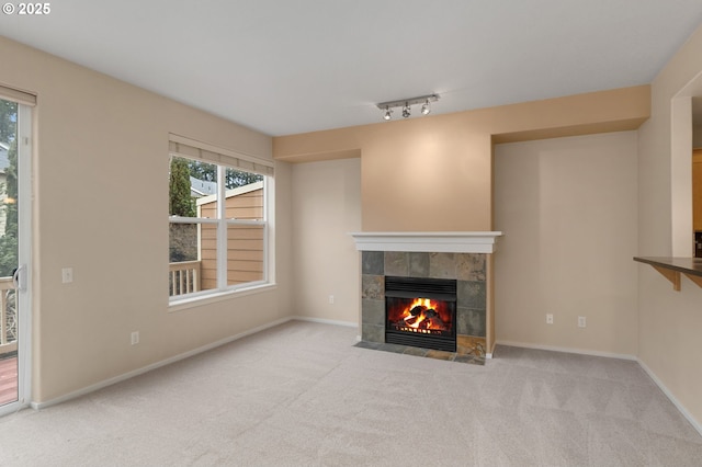 unfurnished living room with carpet, a tile fireplace, rail lighting, and baseboards