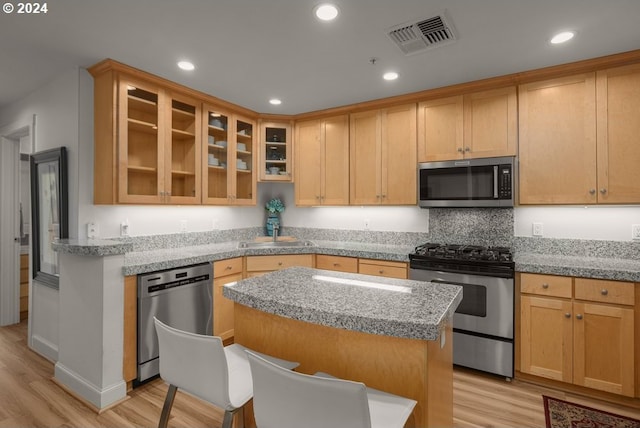 kitchen with light wood-type flooring, sink, a kitchen island, stainless steel appliances, and light stone countertops