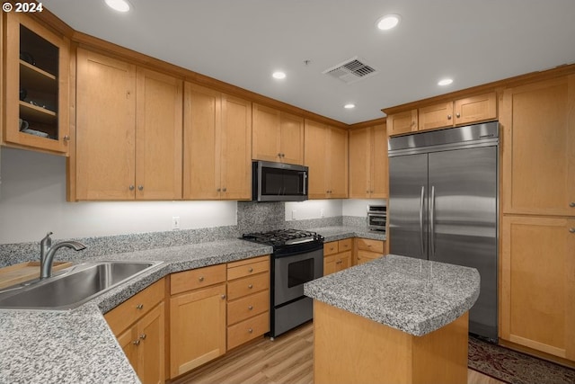 kitchen featuring sink, stainless steel appliances, a center island, light stone countertops, and light hardwood / wood-style floors