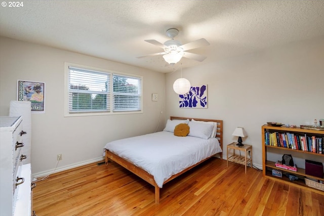 bedroom featuring baseboards, light wood-type flooring, and a textured ceiling