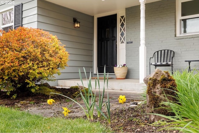 view of exterior entry featuring a porch and brick siding