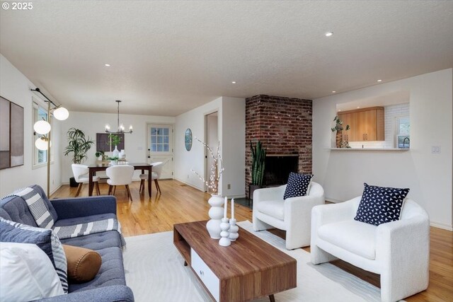 living room featuring a textured ceiling, light hardwood / wood-style floors, a fireplace, and an inviting chandelier