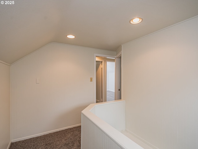 hallway with dark colored carpet and lofted ceiling