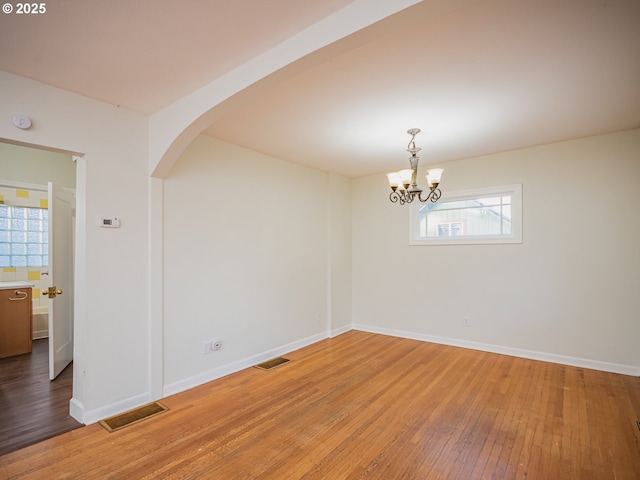 spare room with hardwood / wood-style floors and a notable chandelier