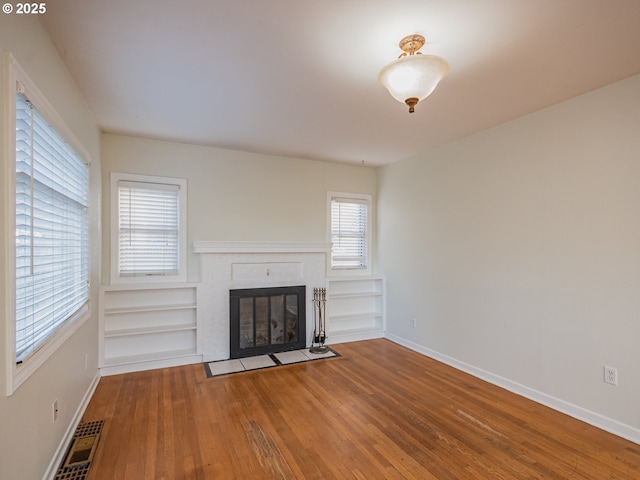 unfurnished living room with a fireplace, built in features, and hardwood / wood-style floors