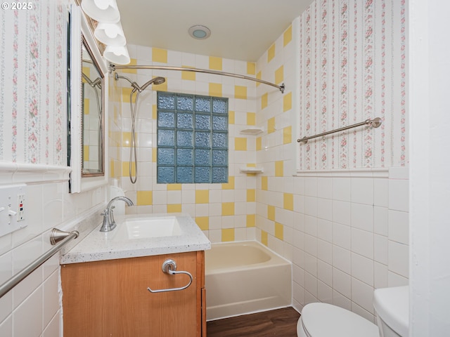 full bathroom featuring hardwood / wood-style floors, vanity, tiled shower / bath combo, toilet, and tile walls