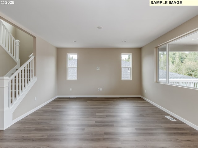 empty room with wood finished floors, stairway, and a healthy amount of sunlight