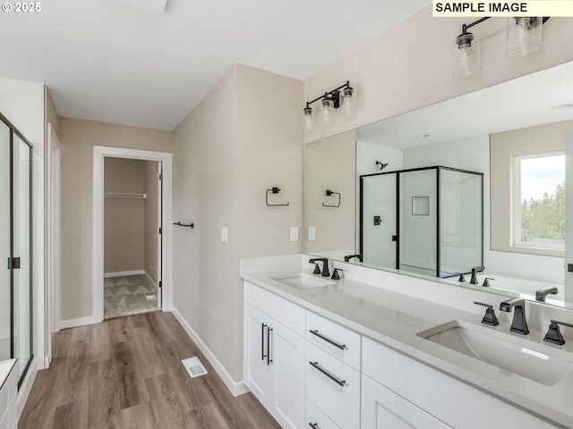 full bathroom featuring a spacious closet, a stall shower, wood finished floors, and a sink