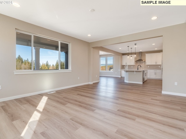 unfurnished living room featuring a sink, light wood-type flooring, baseboards, and recessed lighting