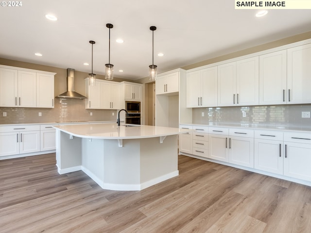 kitchen featuring stainless steel microwave, wall chimney range hood, light wood-type flooring, and a sink