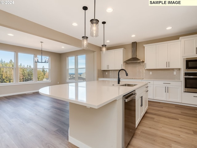 kitchen featuring light wood-style flooring, a sink, wall chimney range hood, appliances with stainless steel finishes, and light countertops