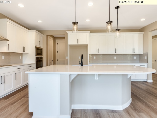 kitchen featuring light wood-style flooring, black appliances, an island with sink, and a sink