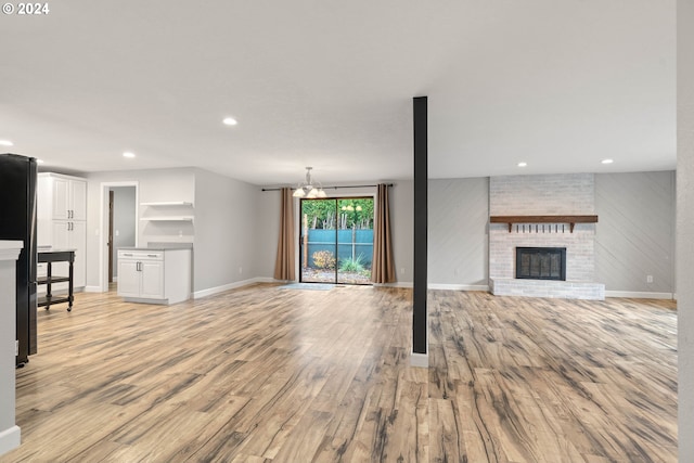 unfurnished living room featuring a notable chandelier, light wood-type flooring, and a brick fireplace