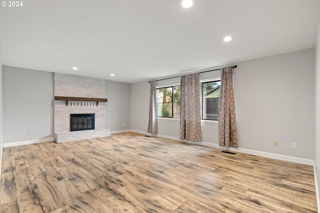 unfurnished living room with a brick fireplace and light hardwood / wood-style flooring