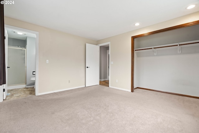 unfurnished bedroom featuring a closet, light carpet, and ensuite bath