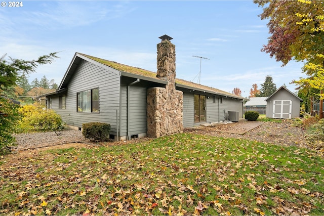 back of property with a storage unit, central AC unit, and a lawn