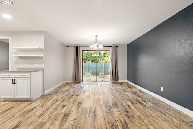 unfurnished dining area featuring light wood-type flooring and an inviting chandelier