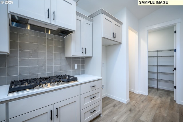 kitchen with light wood-type flooring, tasteful backsplash, vaulted ceiling, stainless steel gas cooktop, and white cabinets